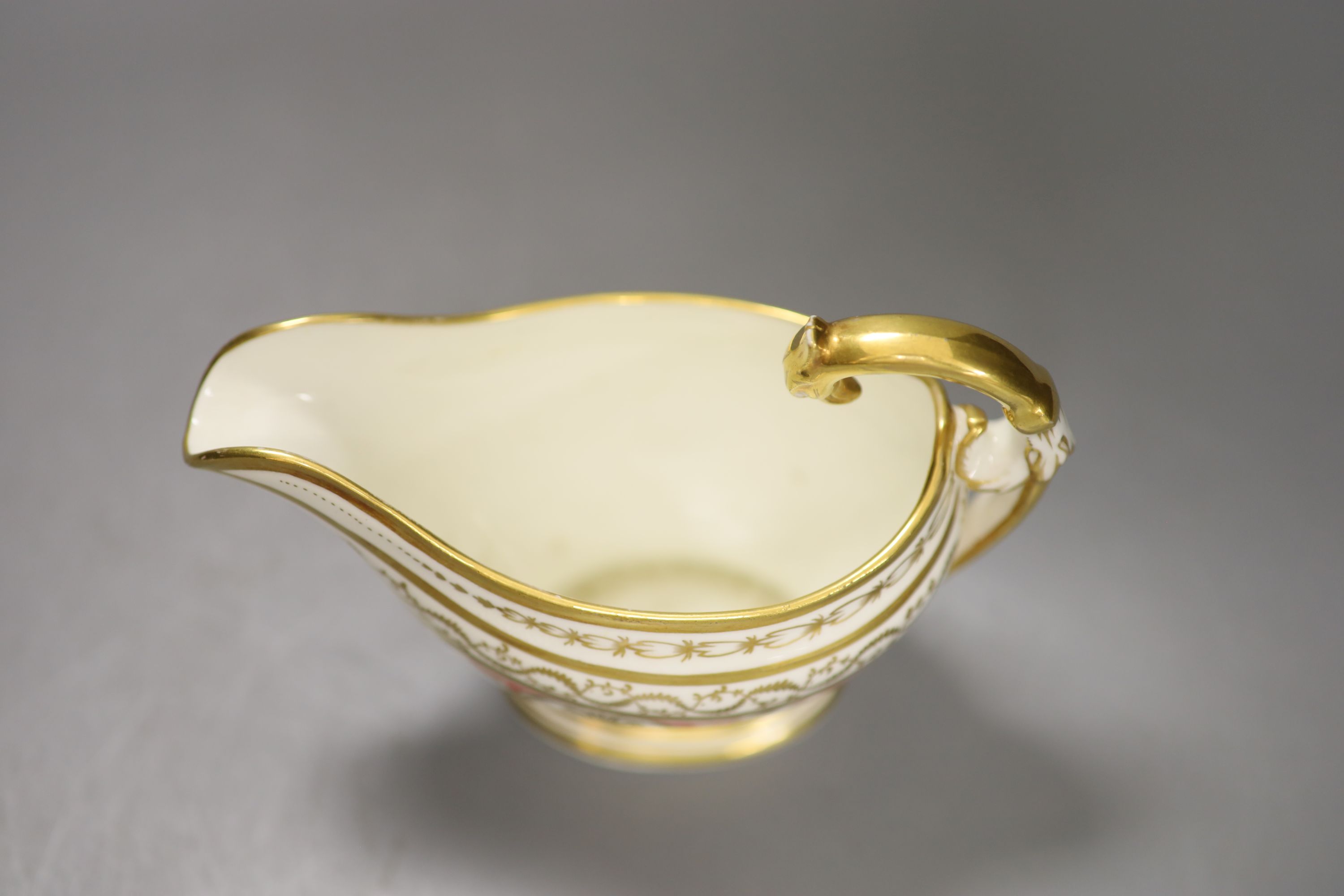 A rare English porcelain sauceboat, with swan neck handle gilded with alternating oval and diamond shaped panels and puce festoons,